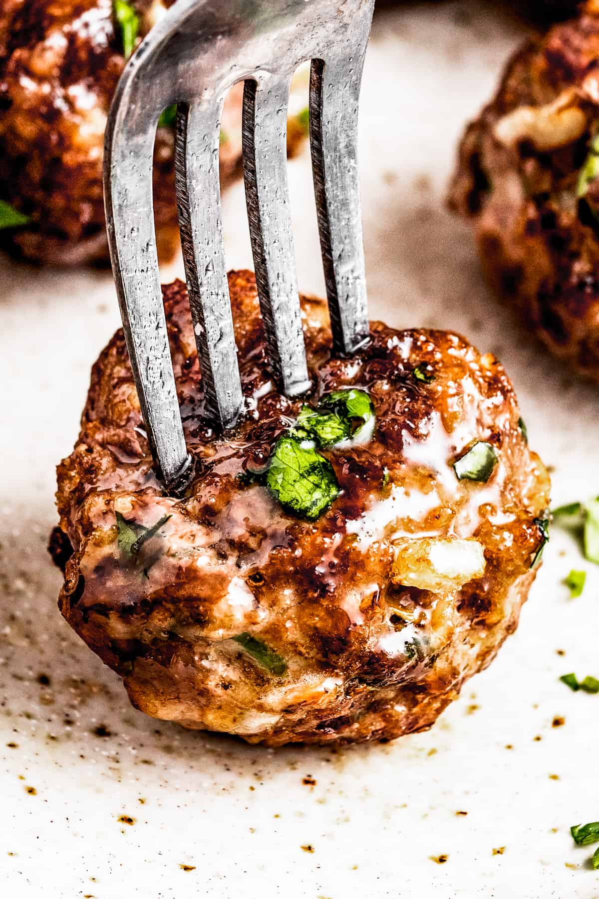 A fork piercing an air fryer meatball served on a plate with other meatballs.