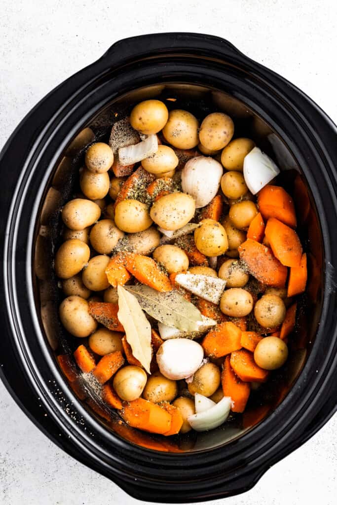Carrots, potatoes, onions, bay leaves, and seasoning in a crock pot.