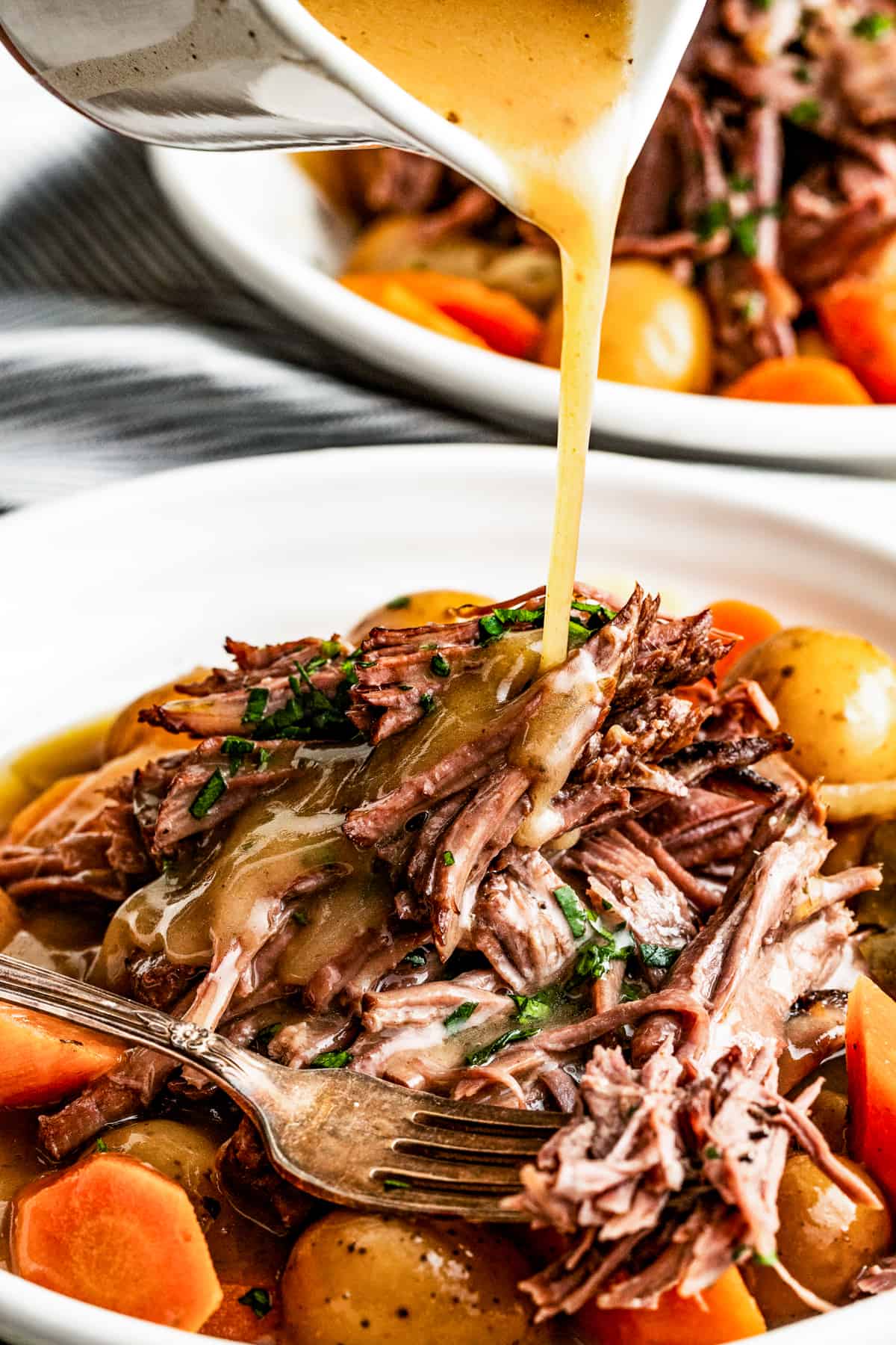 Pouring gravy over crock pot rump roast on a plate with a fork.