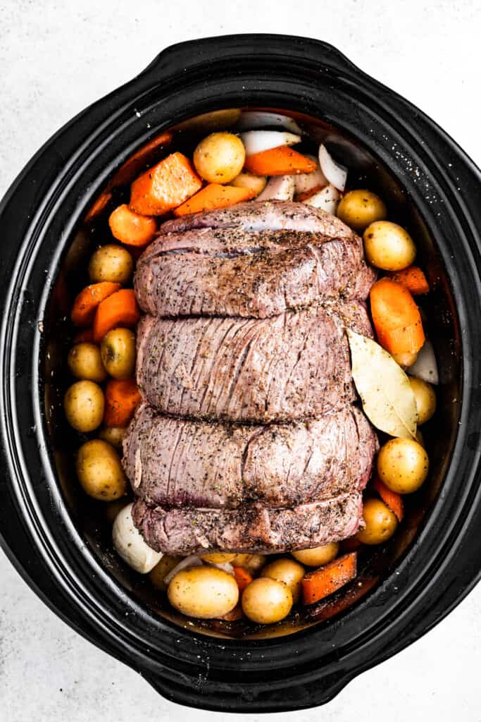 Overhead shot of a rump roast in a crock pot with carrots, potatoes, and onions.