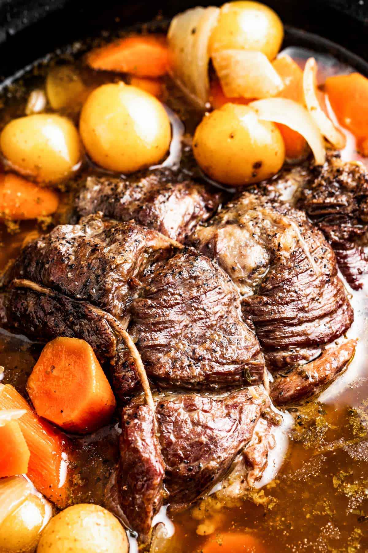 Closeup of crock pot rump roast in a crock pot, surrounded with gold baby potatoes and sliced carrots.