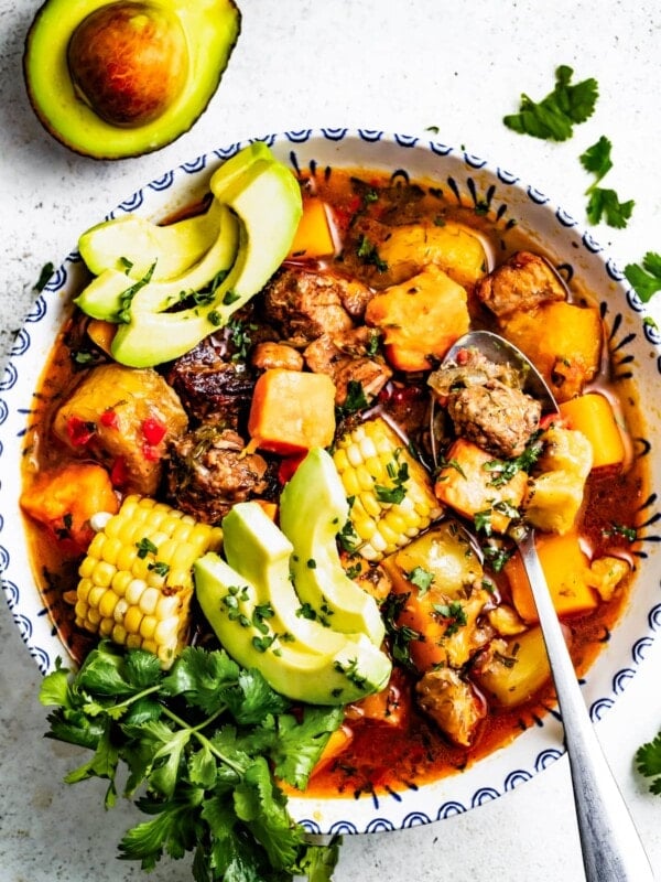 Overhead image of Sancocho Dominicano served in a bowl topped with avocado and cilantro near an avocado half.