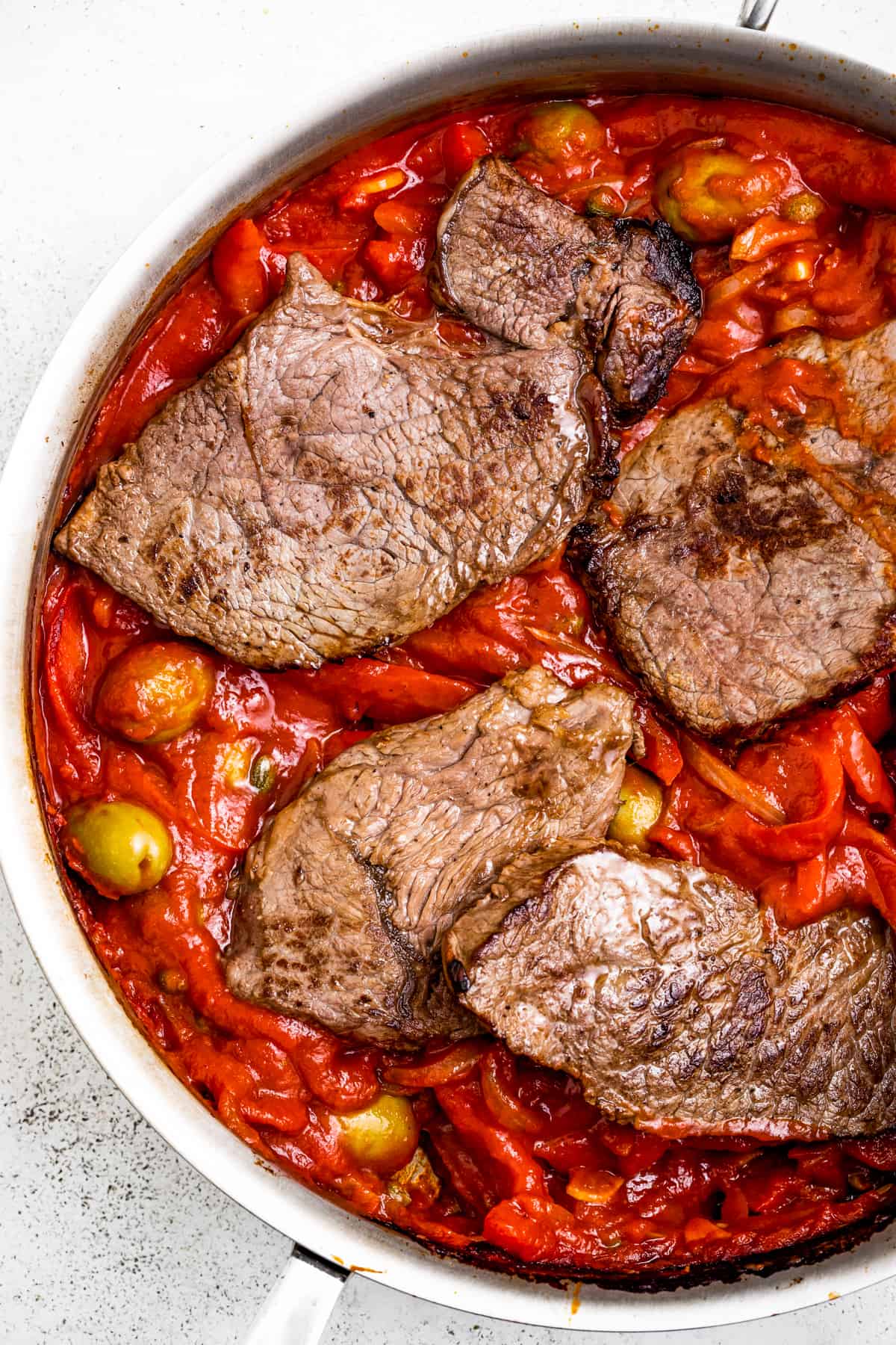 Adding seared steak to a pan full of tomato sauce and veggies.