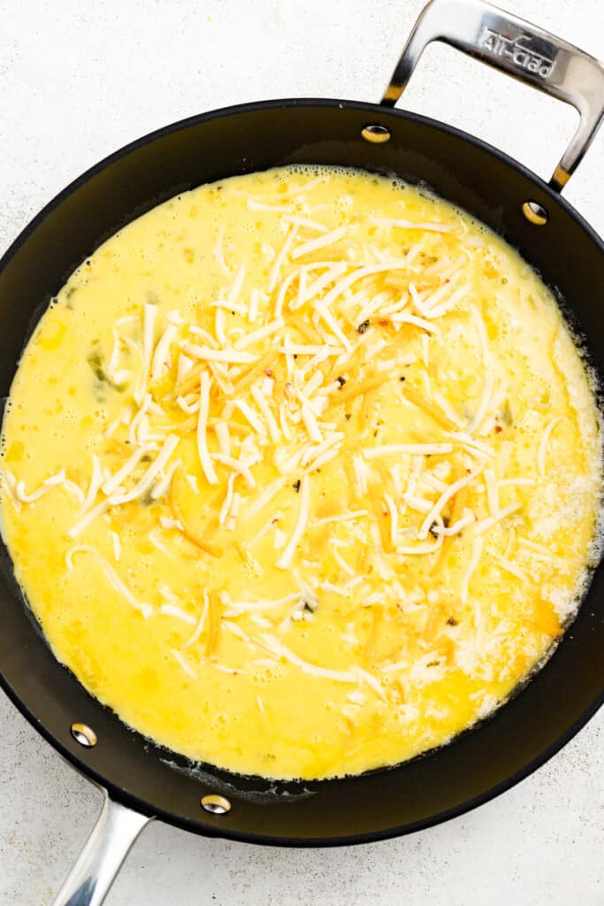 Adding cheese to beaten eggs and milk in a pan.