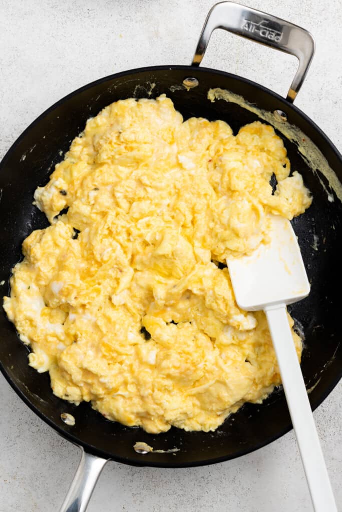 Cheesy scrambled eggs in a pan with a rubber spatula.