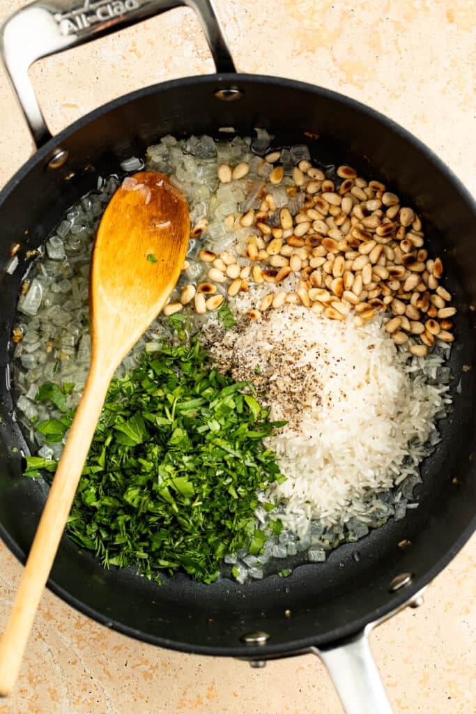 Combining cooked onions and garlic with fresh herbs, toasted pine nuts, soaked rice, lemon juice, and seasoning.