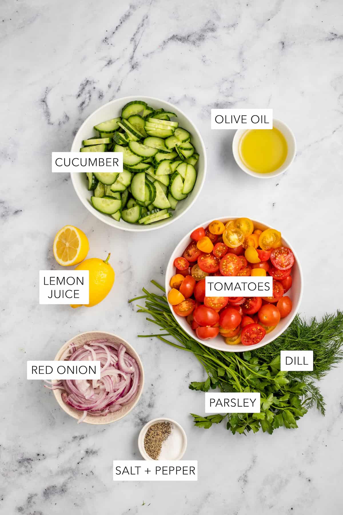 Ingredients for tomato and cucumber salad separated into bowls and labeled.