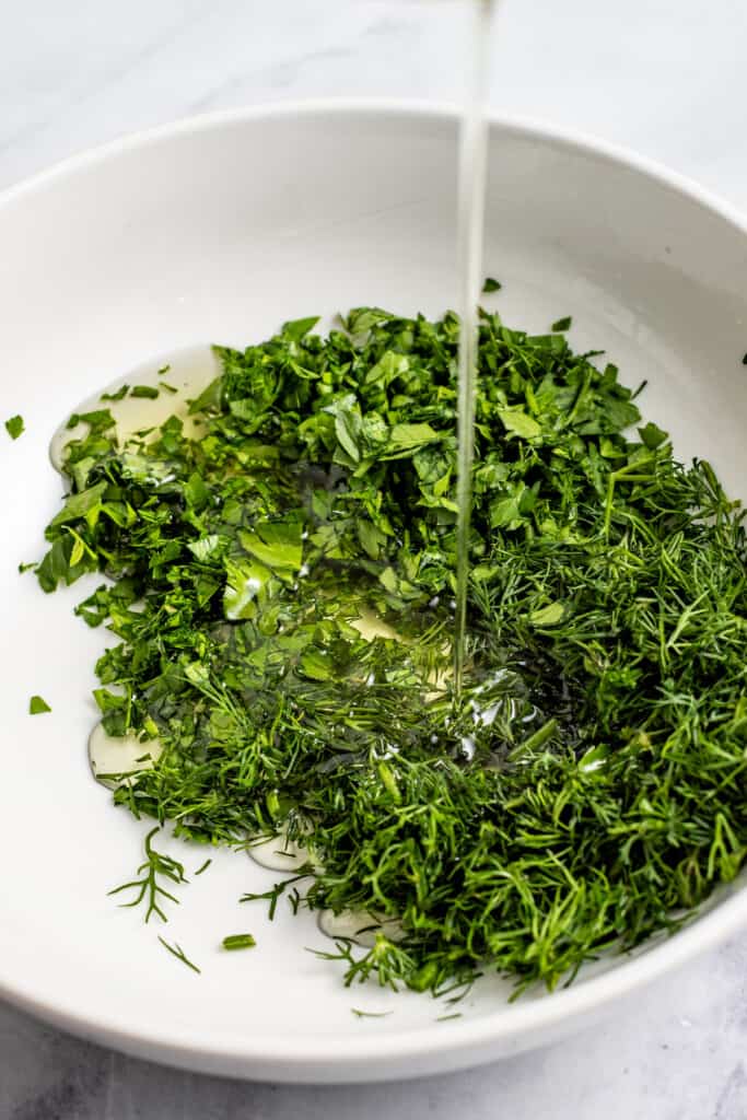 Adding olive oil and lemon juice to fresh herbs to make salad dressing.