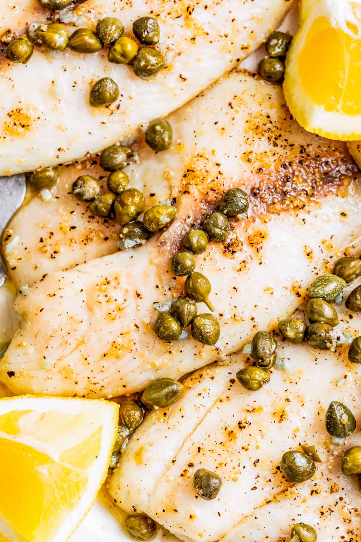 Tilapia cooked in the air fryer and arranged on a serving platter with lemon caper sauce and fresh lemons.