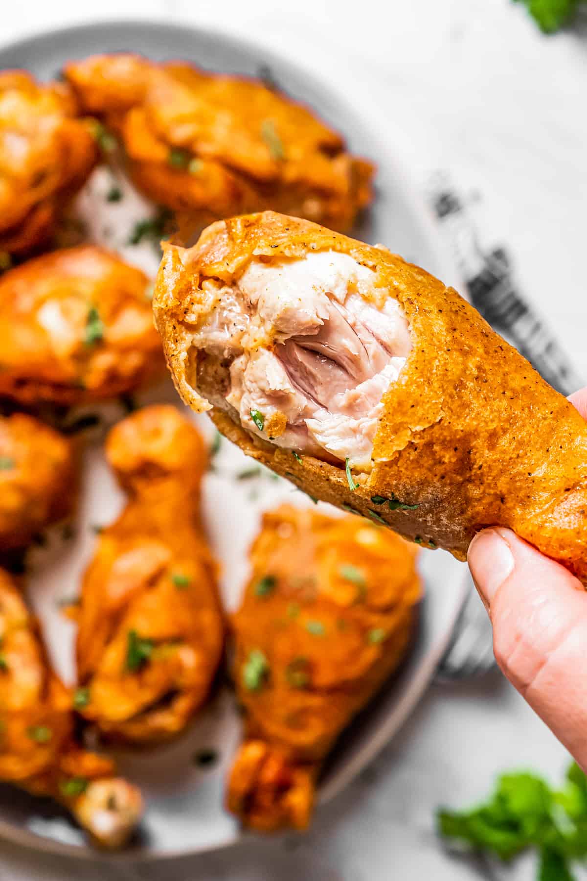 Female hand holding up a beer-battered chicken drumstick with a bite taken out of it.