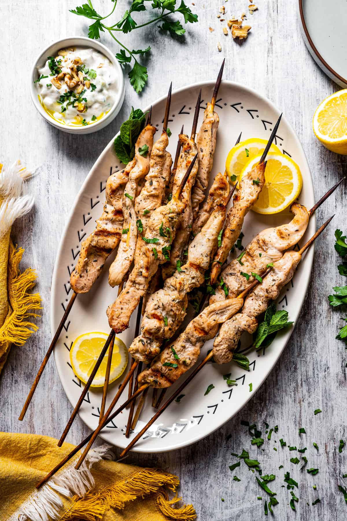 A serving plate with cooked chicken skewers and lemon wedges