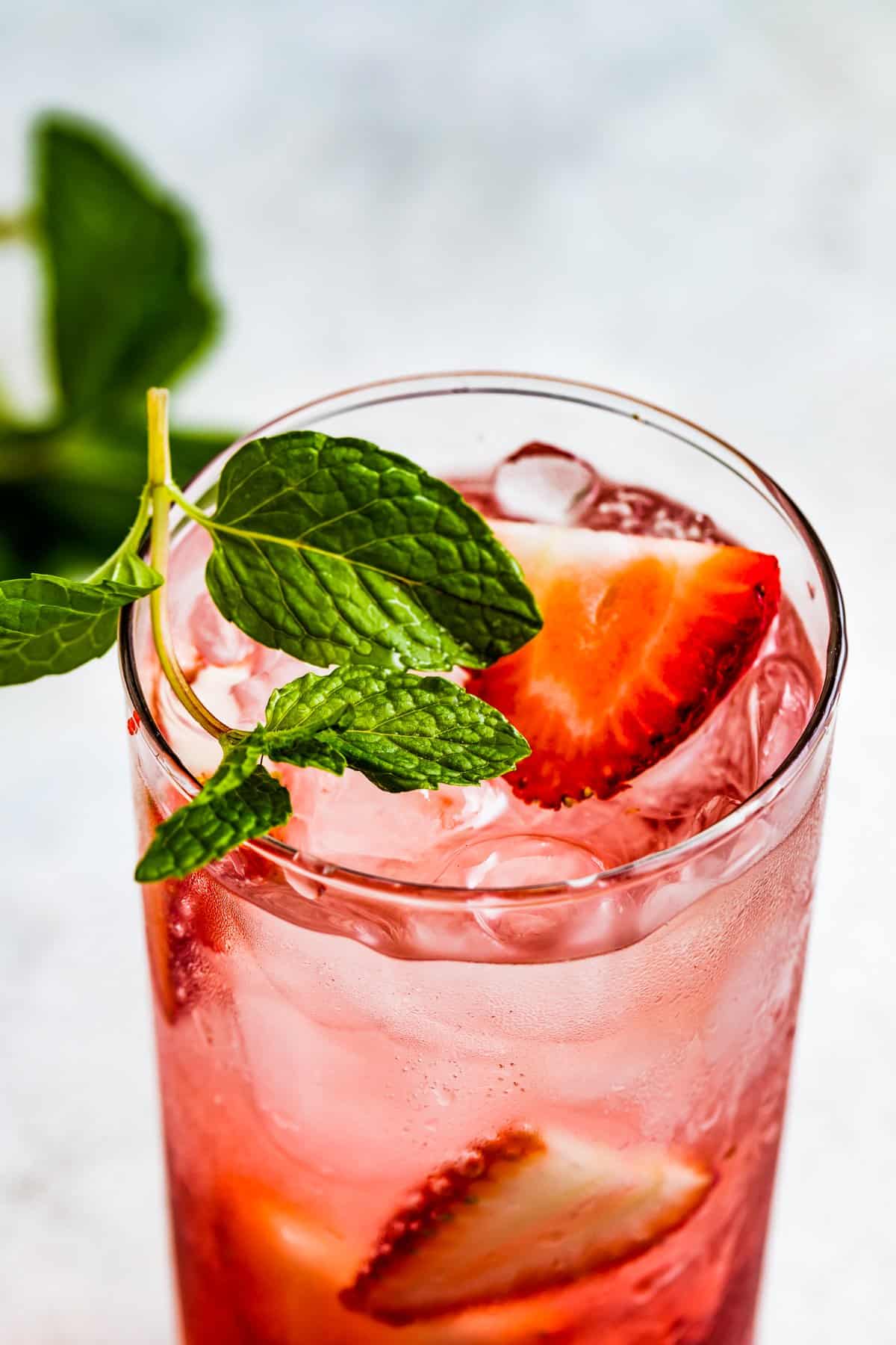 Close-up of a drinking glass filled with iced tea, strawberries, and a garnish of mint.