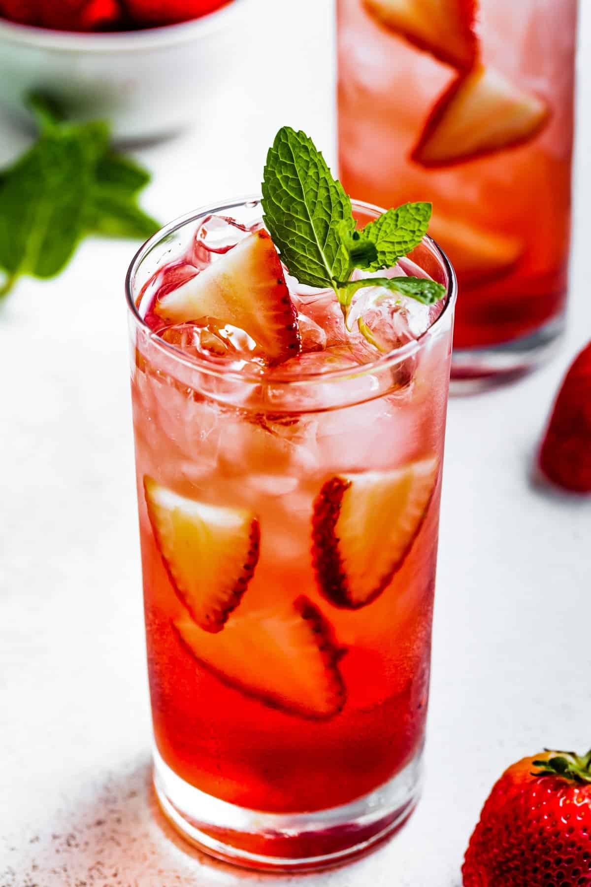 Highball glass with hibiscus iced tea garnished with mint and strawberries.