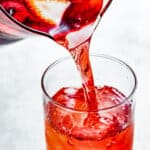 Pouring hibiscus iced tea from a pitcher into a drinking glass.