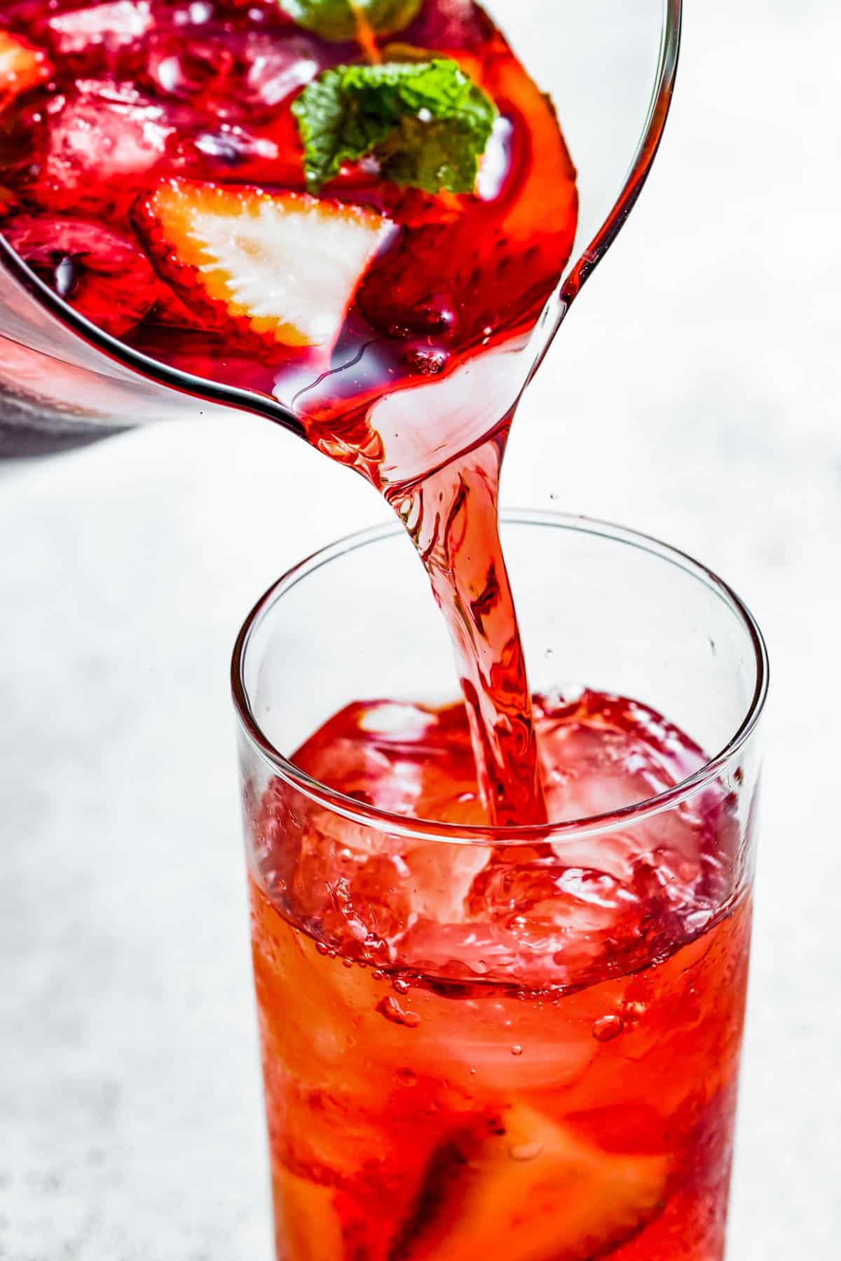 Pouring hibiscus iced tea from a pitcher into a drinking glass.