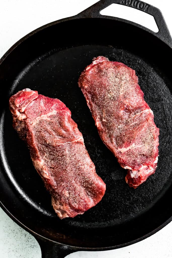 Searing two fillet of New York steak in a pan.