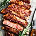 Sliced New York strip steak with fresh rosemary near a steak knife.