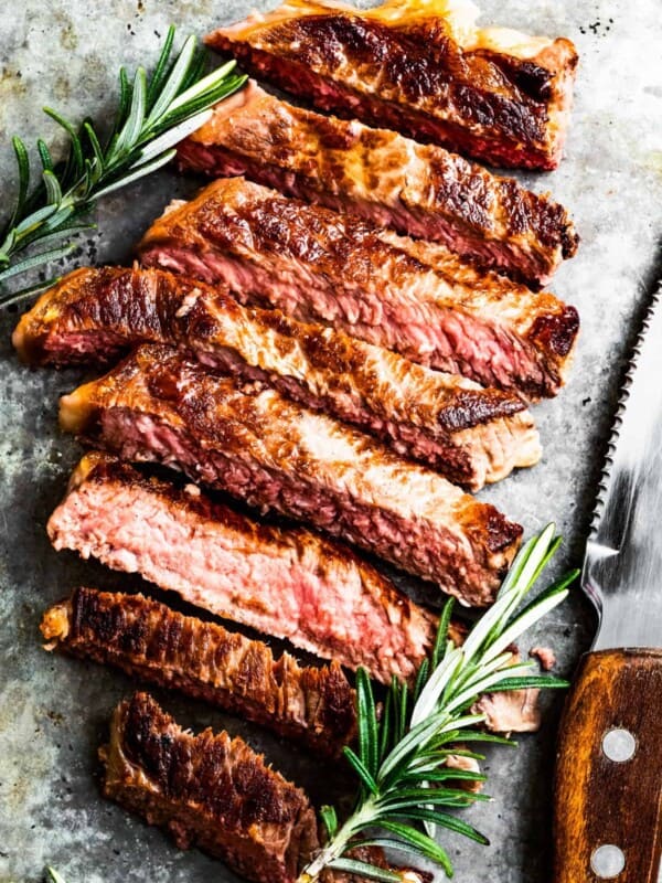 Sliced New York strip steak with fresh rosemary near a steak knife.