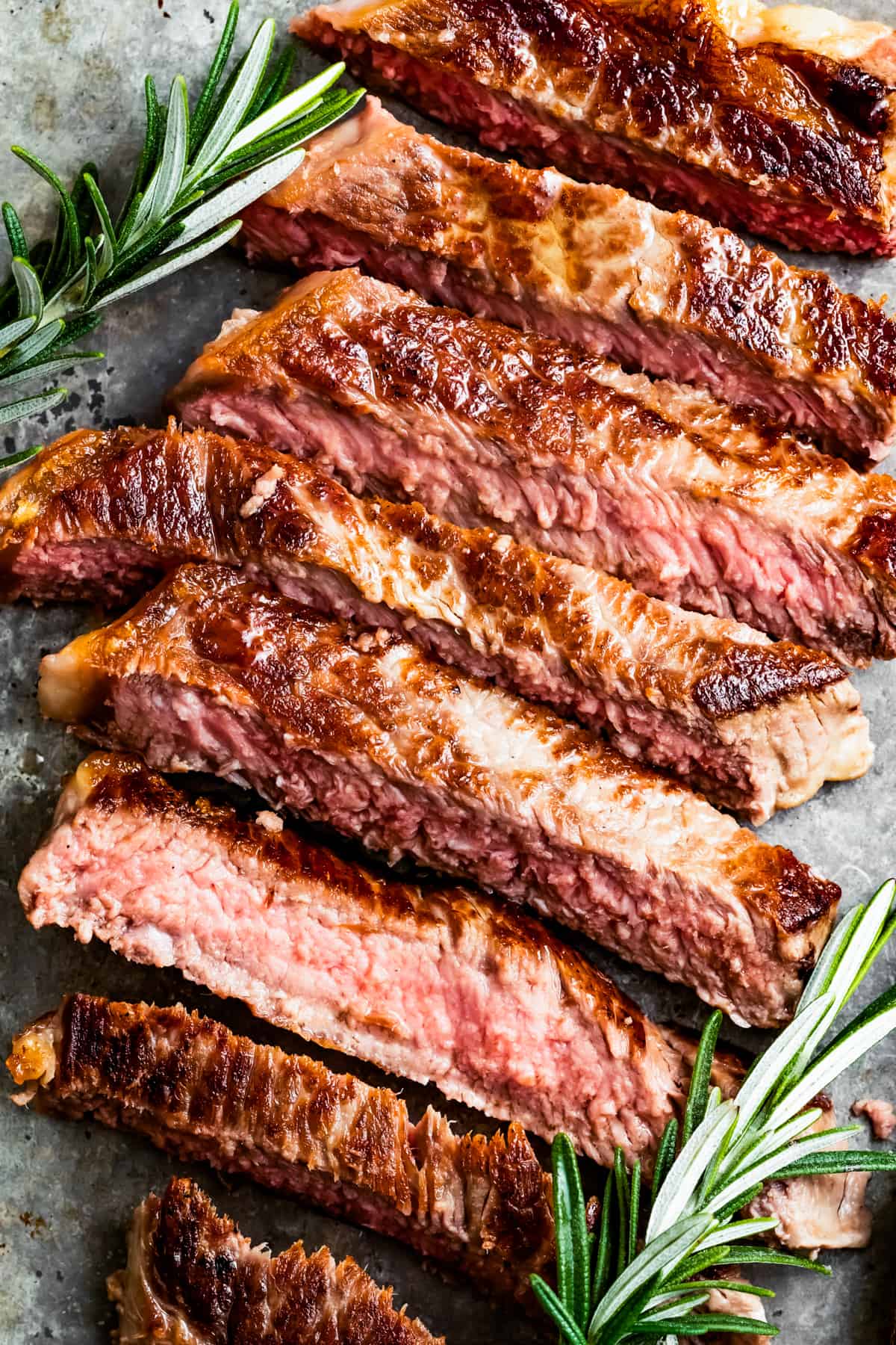 Sliced New York strip steak with fresh rosemary sprigs set next to it.