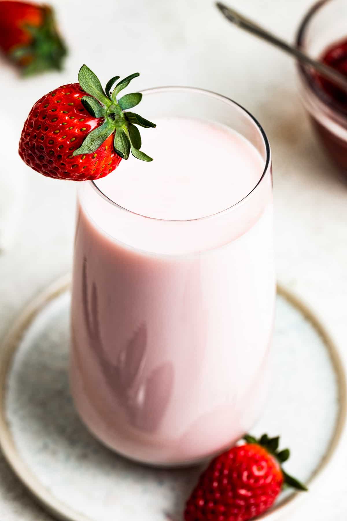 Strawberry milk in a glass with a strawberry on the edge of the glass.