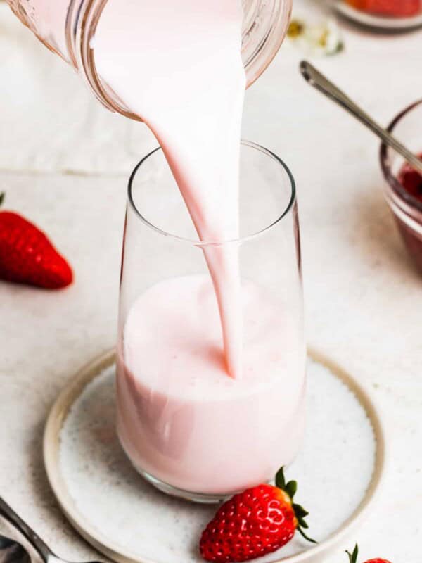 Pouring strawberry milk into a glass.