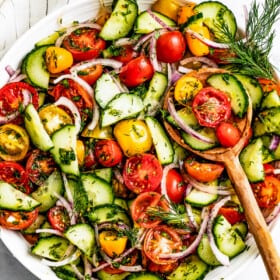 Tomato and cucumber salad in a serving bowl with a wooden spoon.