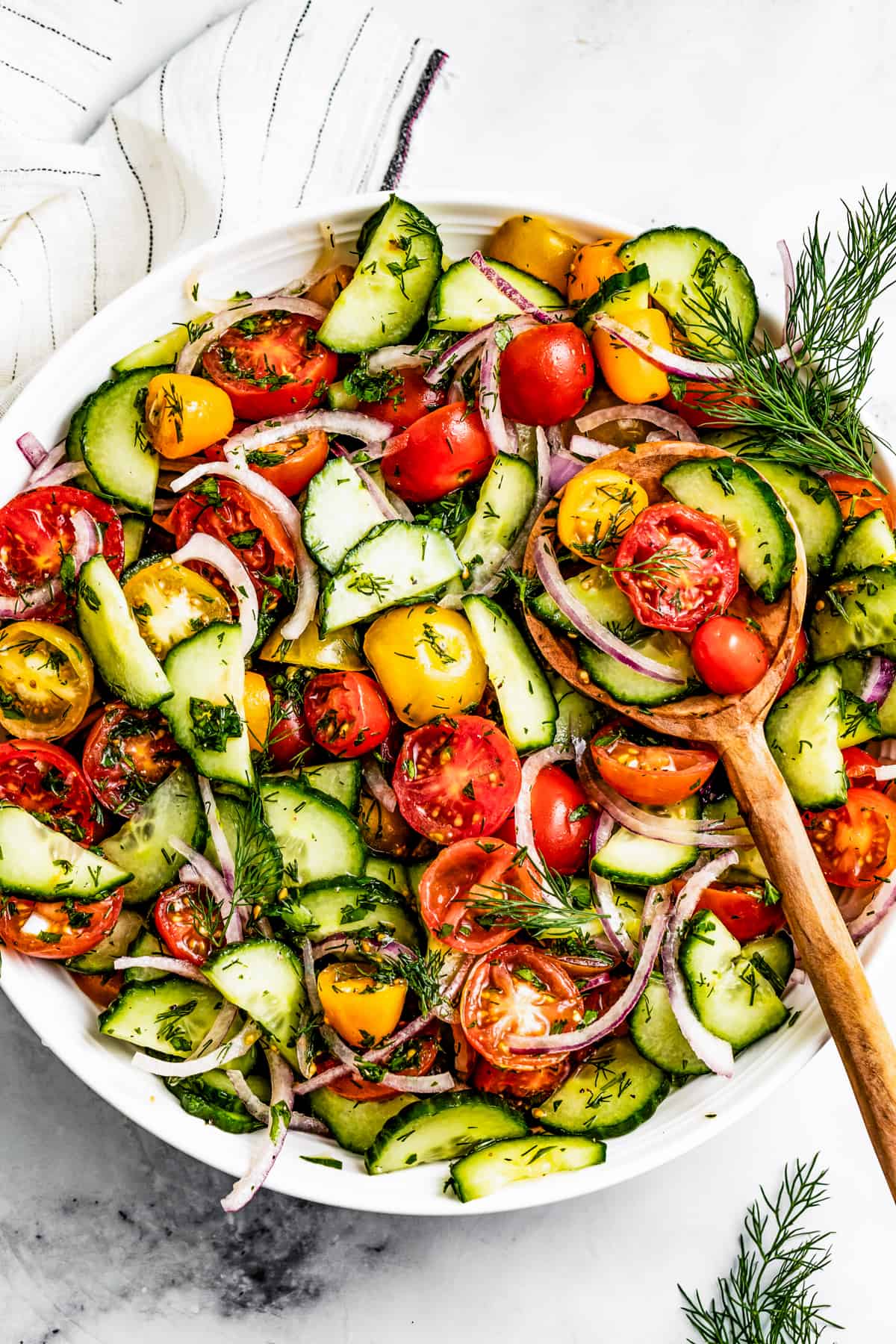 Tomato and cucumber salad in a serving bowl with a wooden spoon.