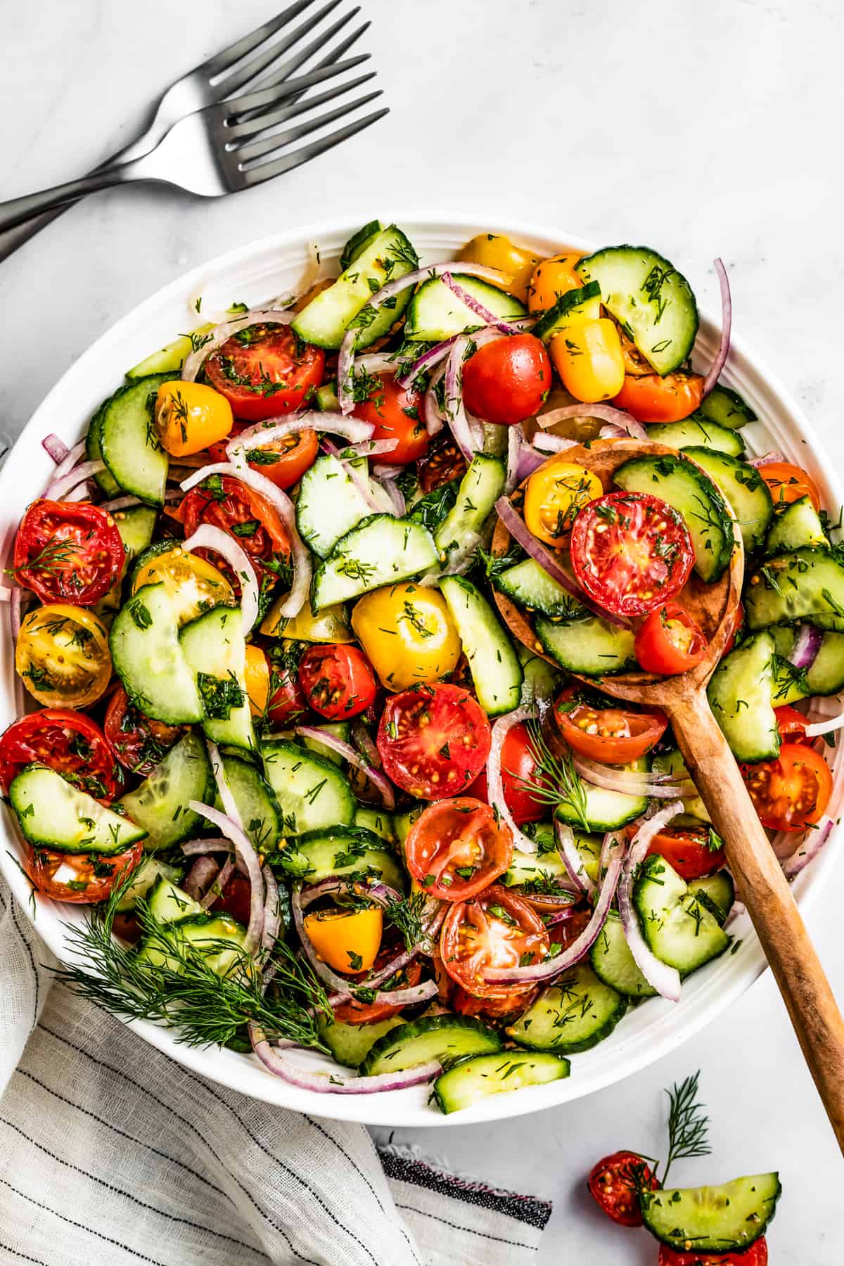 Tomato and cucumber salad in a serving bowl with a wooden spoon.