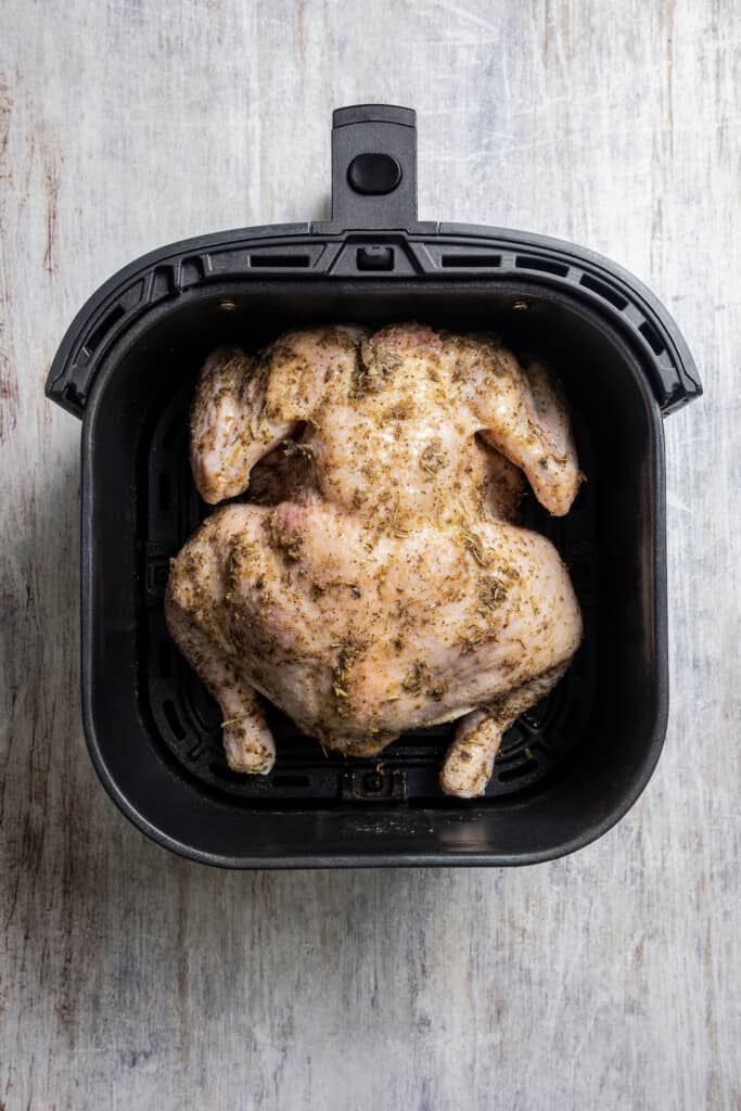 Placing seasoned chicken, breast-side down, in the basket of an air fryer.