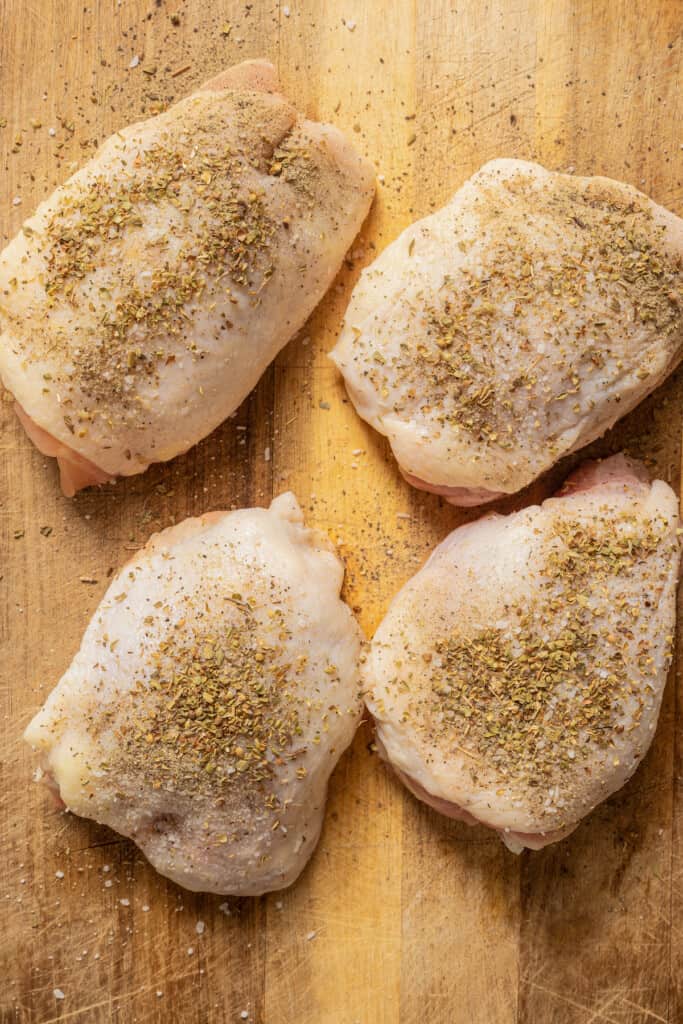 Seasoning chicken thighs with salt, pepper, and oregano.