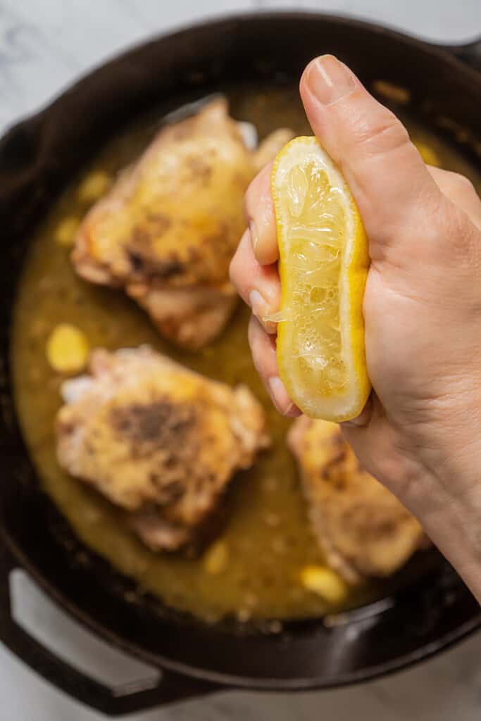 Squeezing lemon juice into a pan with chicken in white wine sauce.