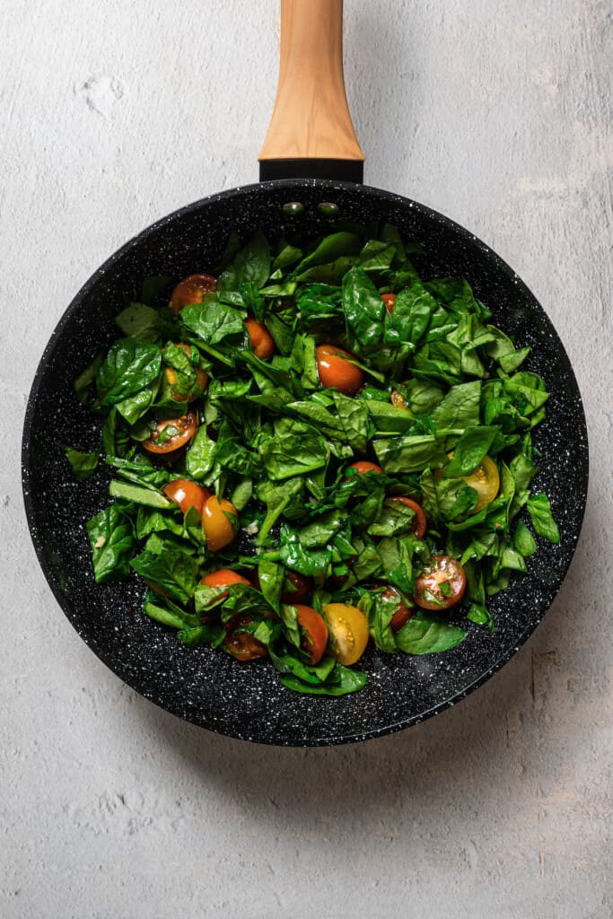 Adding spinach to a pan of sautéed tomatoes and garlic.