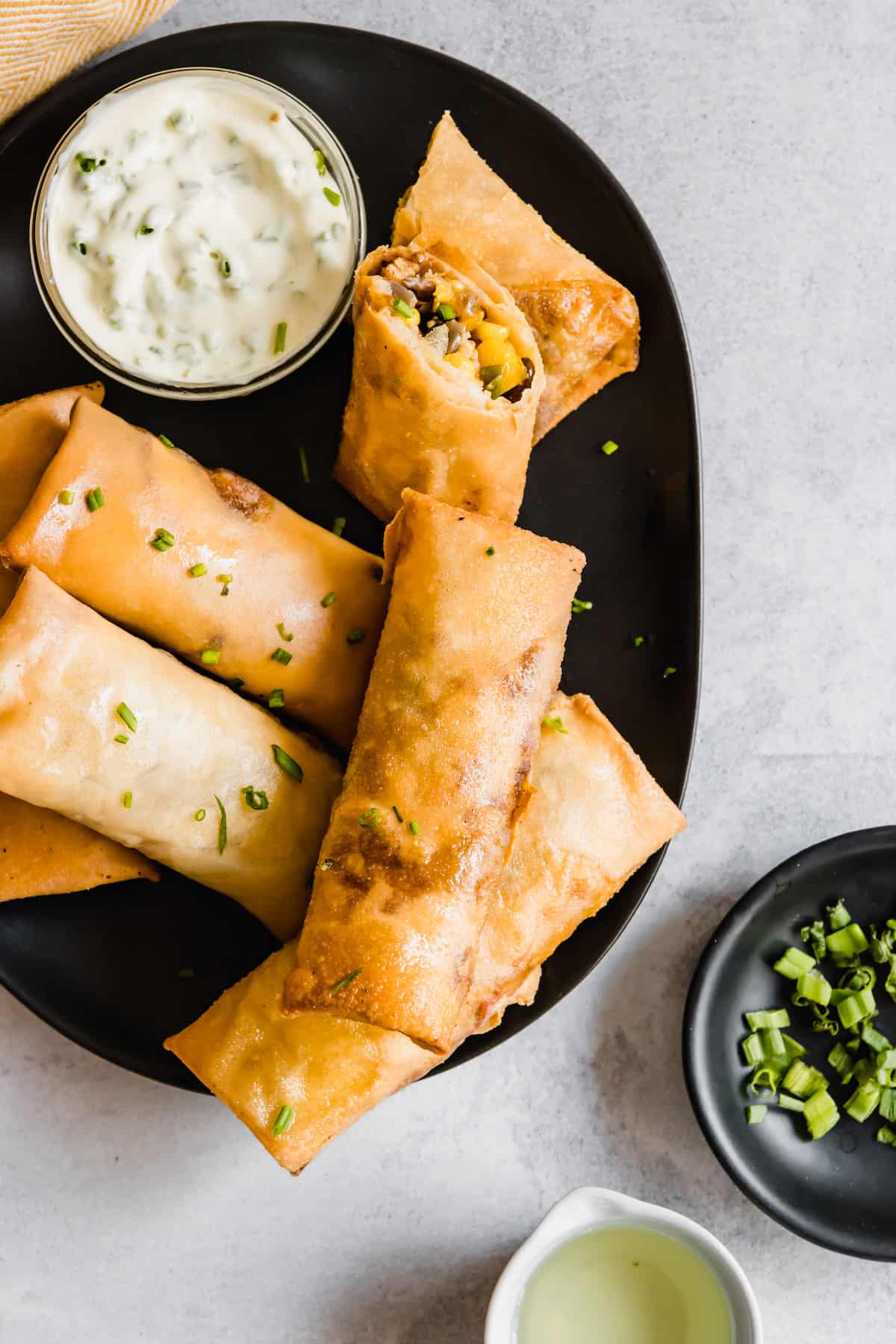 tex mex egg rolls arranged on a black plate with a white sauce in a bowl.