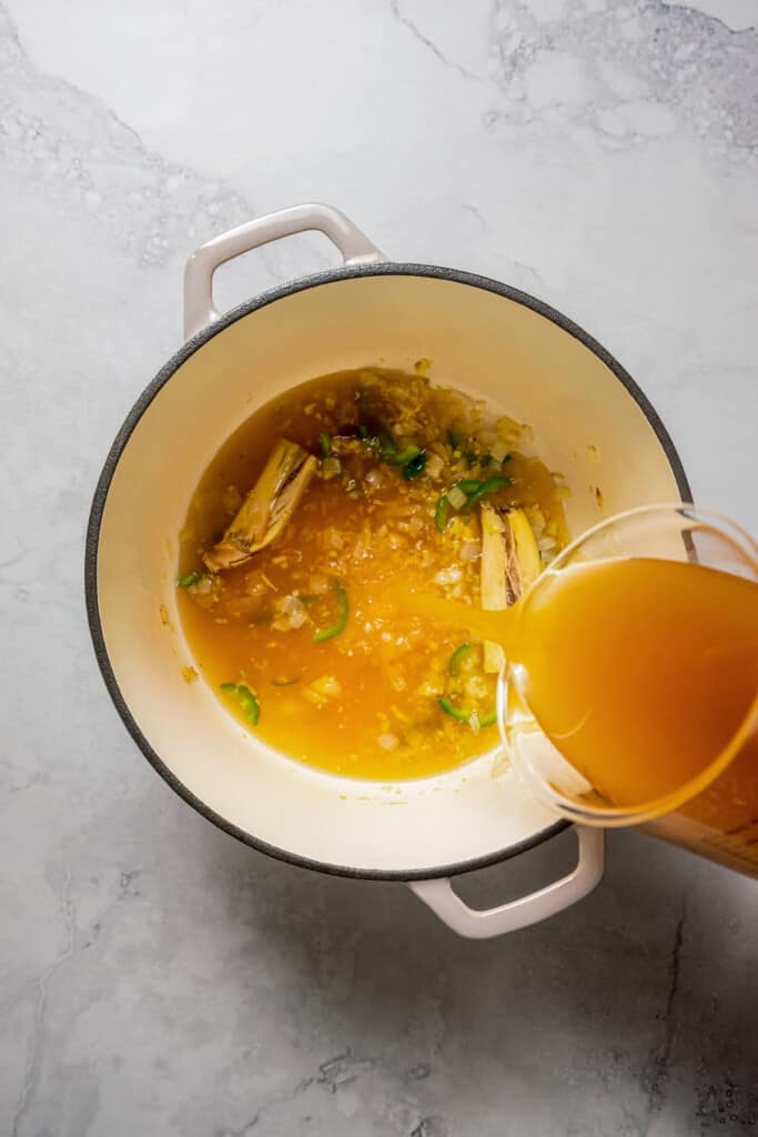 Adding chicken stock to aromatics for tom yum broth.