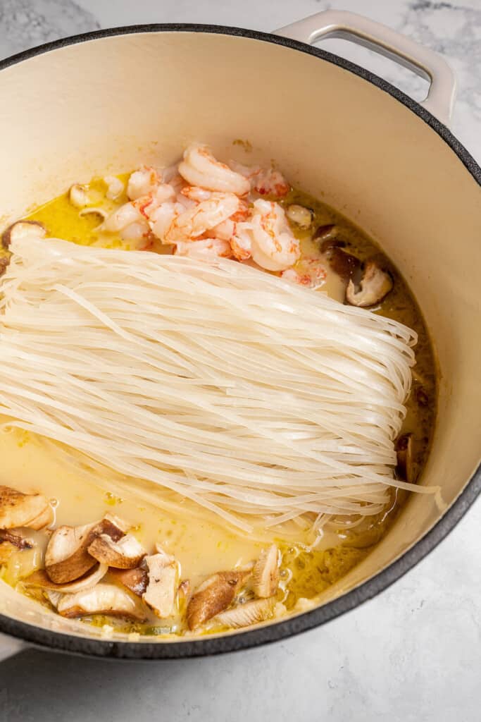 Adding mushrooms, shrimp, and noodles to tom yum broth.
