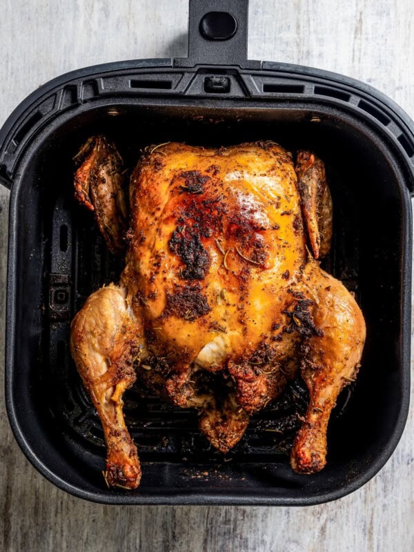 A whole crispy chicken in the basket of an air fryer.