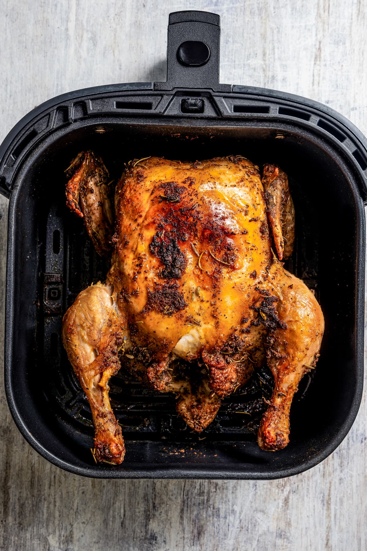 A whole crispy chicken in the basket of an air fryer.