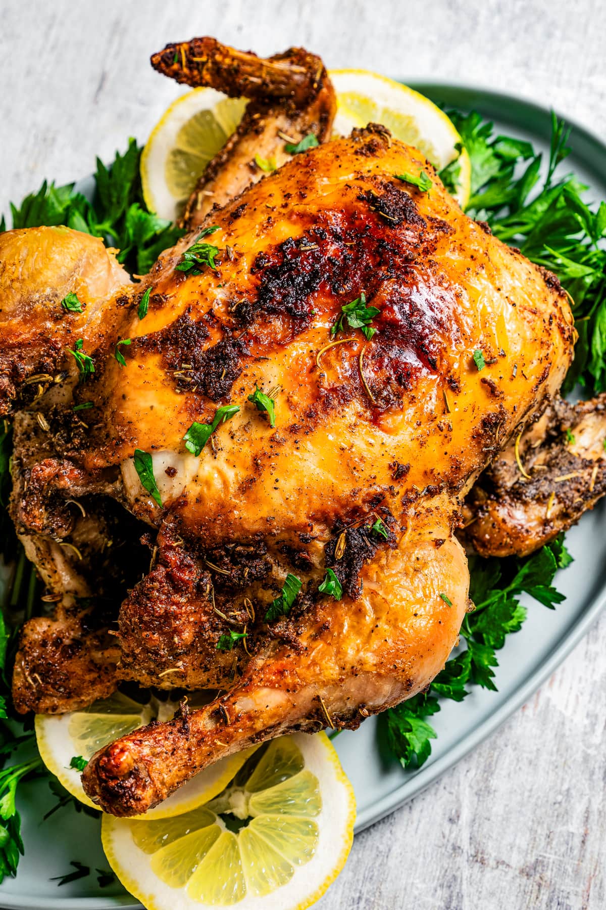 Image of air fryer rotisserie chicken on a serving platter over fresh herbs and lemon.