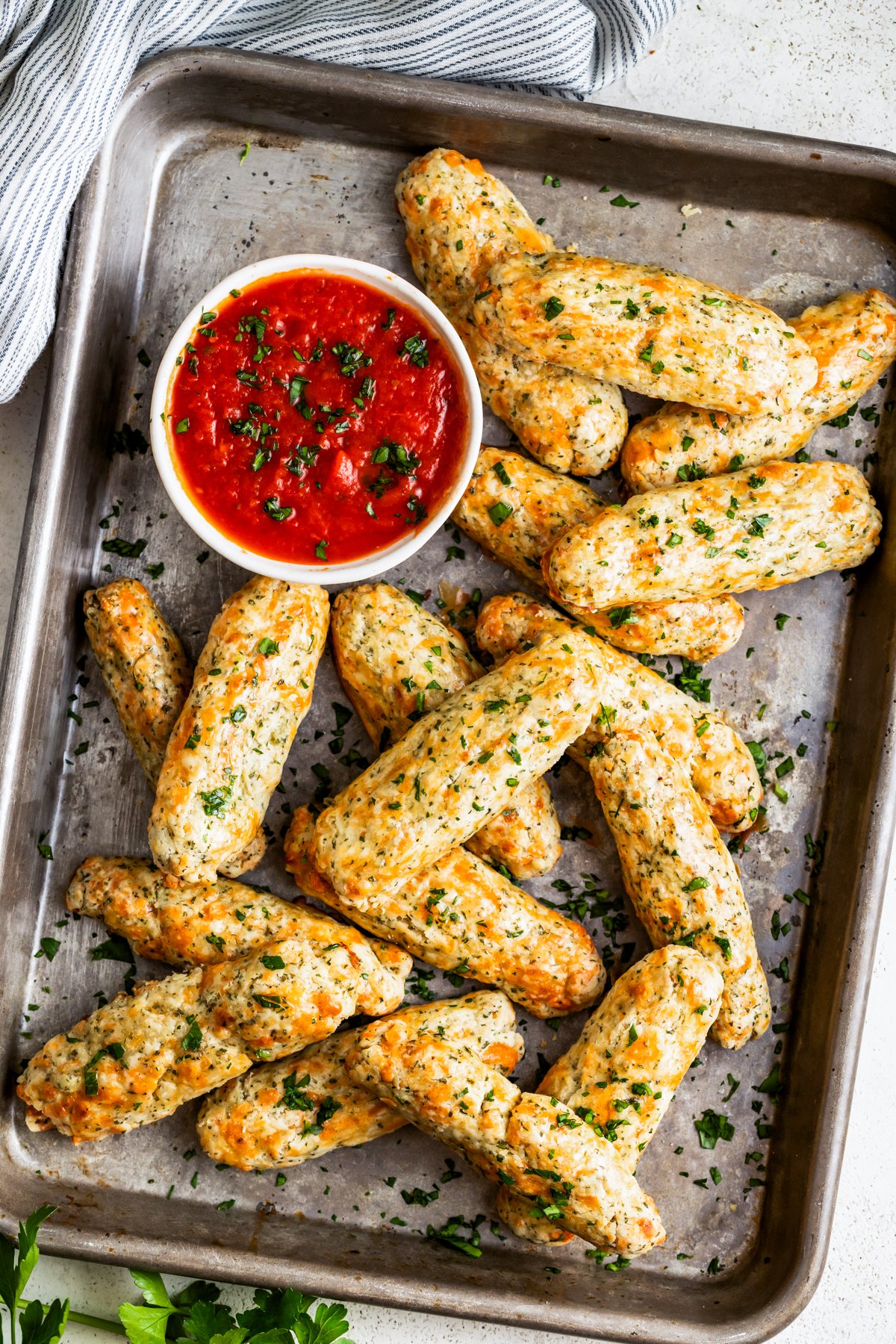 Wide overhead shot of homemade baked mozzarella sticks on a tray with a bowl of marinara sauce.