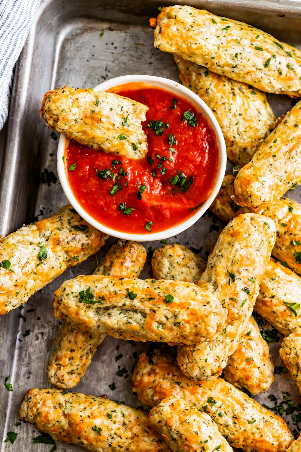 Overhead shot of homemade baked mozzarella sticks on a tray with a bowl of marinara sauce.