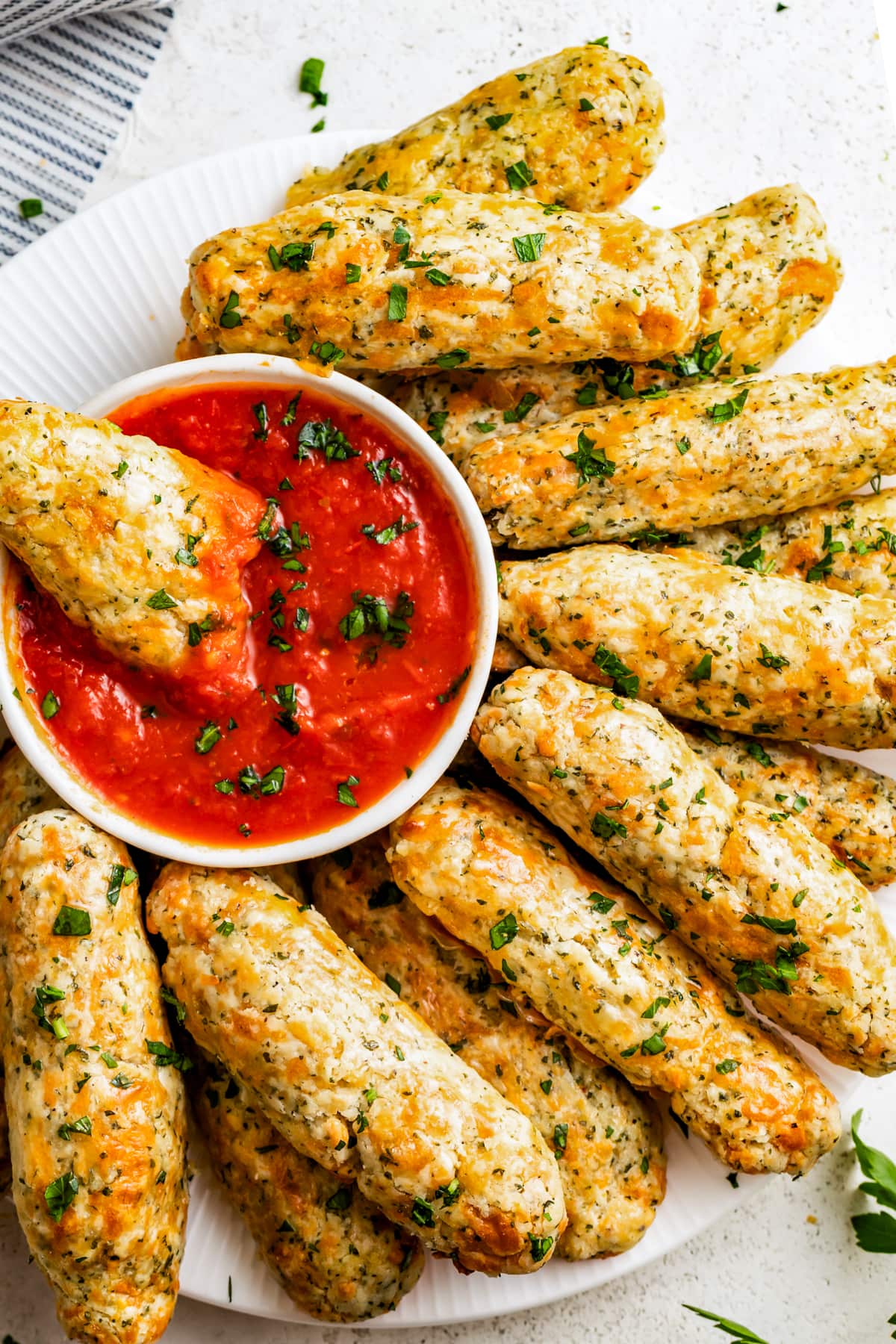 Dipping a mozzarella stick into a bowl of marinara sauce on a plate with other mozzarella sticks.