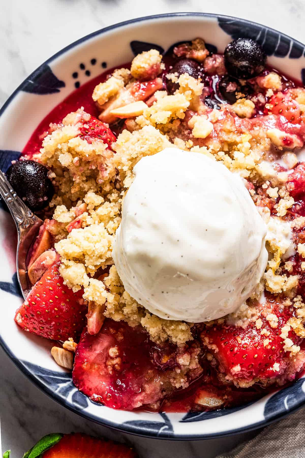 Overhead close-up shot of a bowl with blueberry strawberry crumble, and a scoop of vanilla ice cream on top.