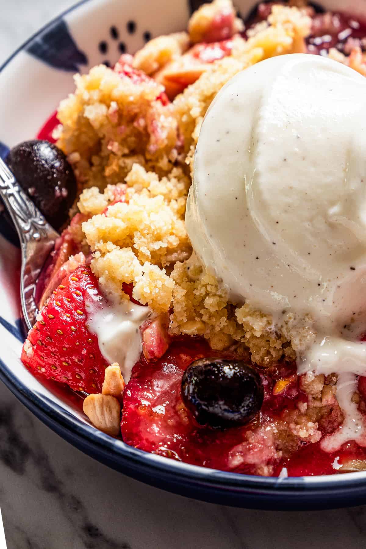 Side shot close-up of a bowl with blueberry strawberry crumble, and a scoop of vanilla ice cream on top.
