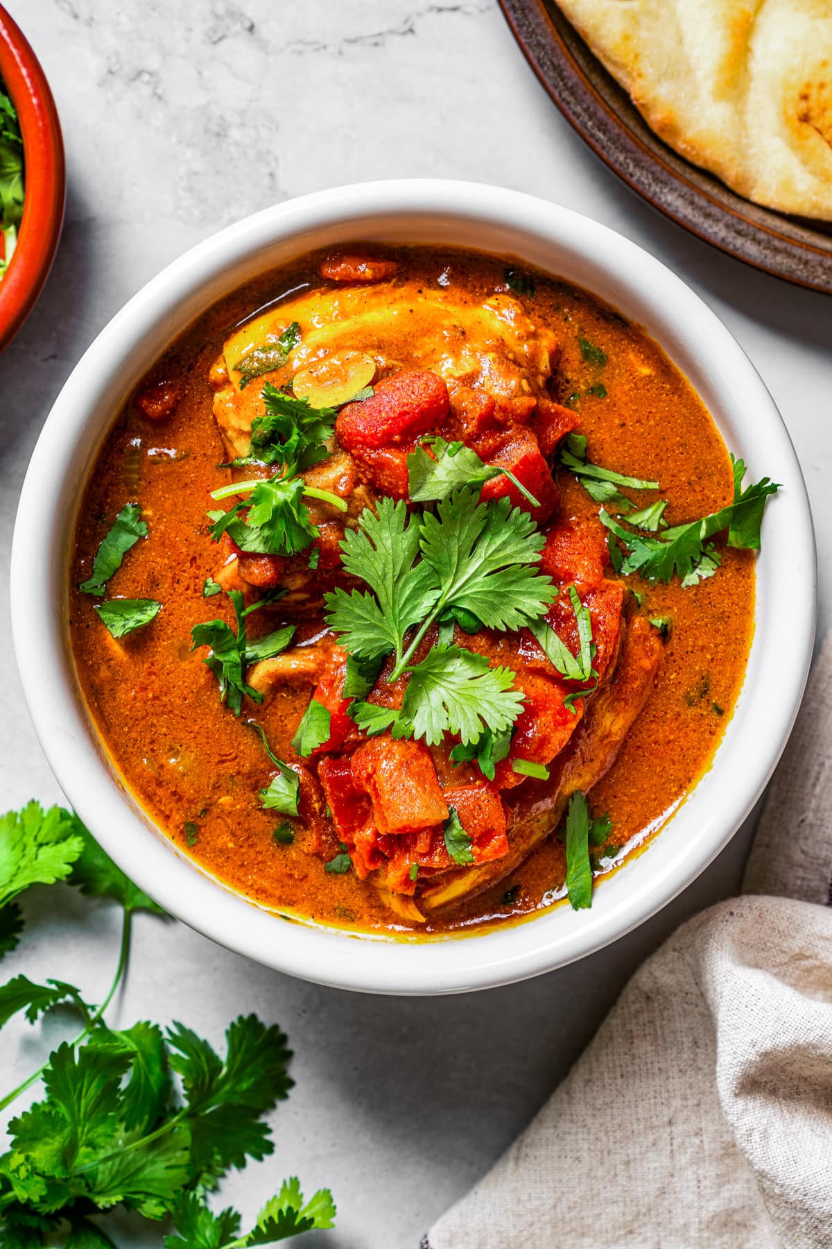 Image of a bowl of chicken rogan josh near fresh cilantro and naan.