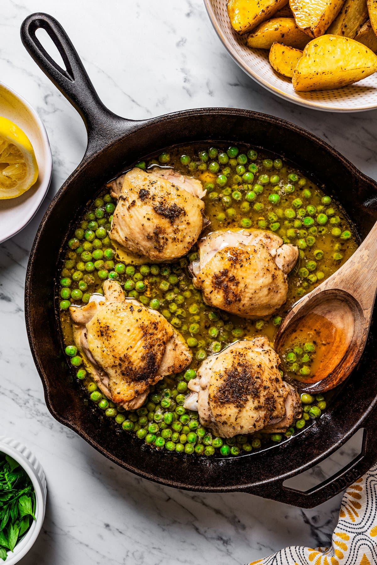 Chicken and peas in lemony sauce in a pan near a bowl of roasted potatoes.