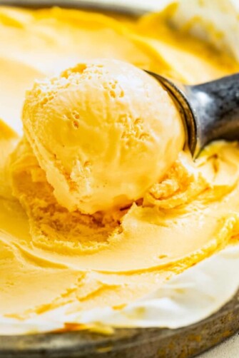 Scooping mango ice cream out of a glass a container with an ice cream scoop.