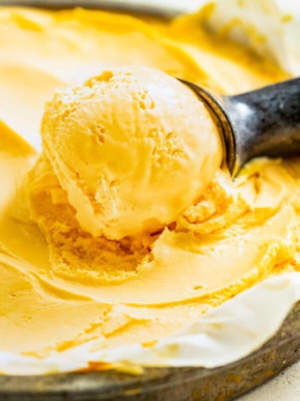 Scooping mango ice cream out of a glass a container with an ice cream scoop.