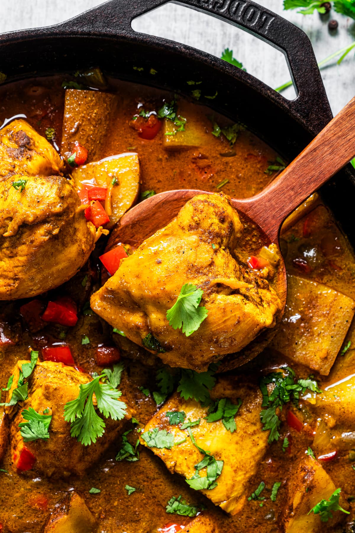 Closeup of Jamaican curry chicken in a pan with a wooden spoon.