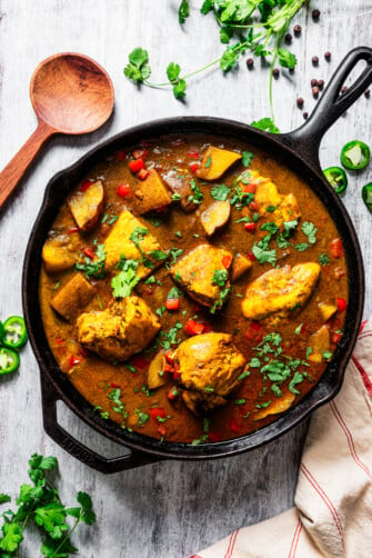 Jamaican curry chicken in a pan near a wooden spoon.