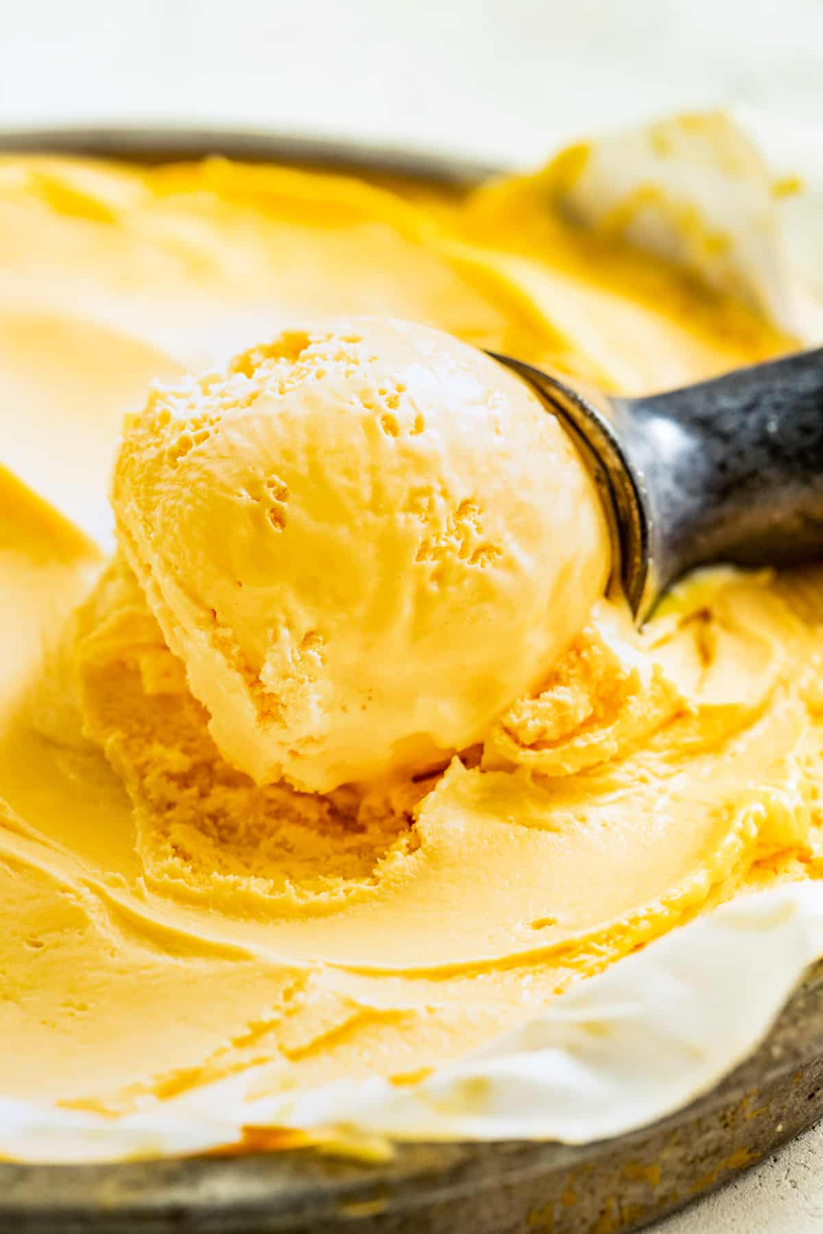 Scooping mango ice cream out of a glass a container with an ice cream scoop.